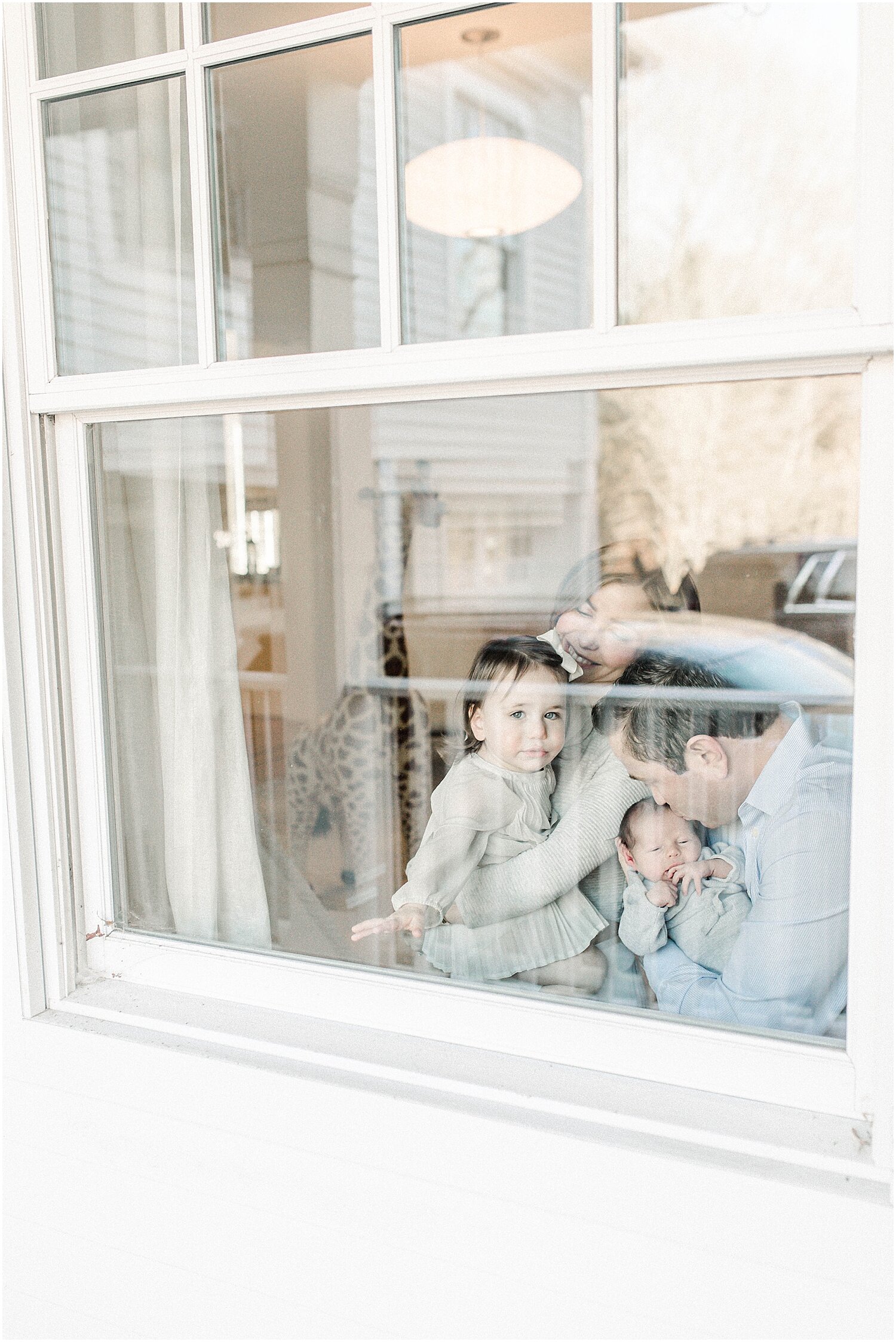 Photo of family through the window during in-home lifestyle newborn photoshoot in Westport, CT. Photos by Connecticut Newborn Photographer, Kristin Wood Photography.