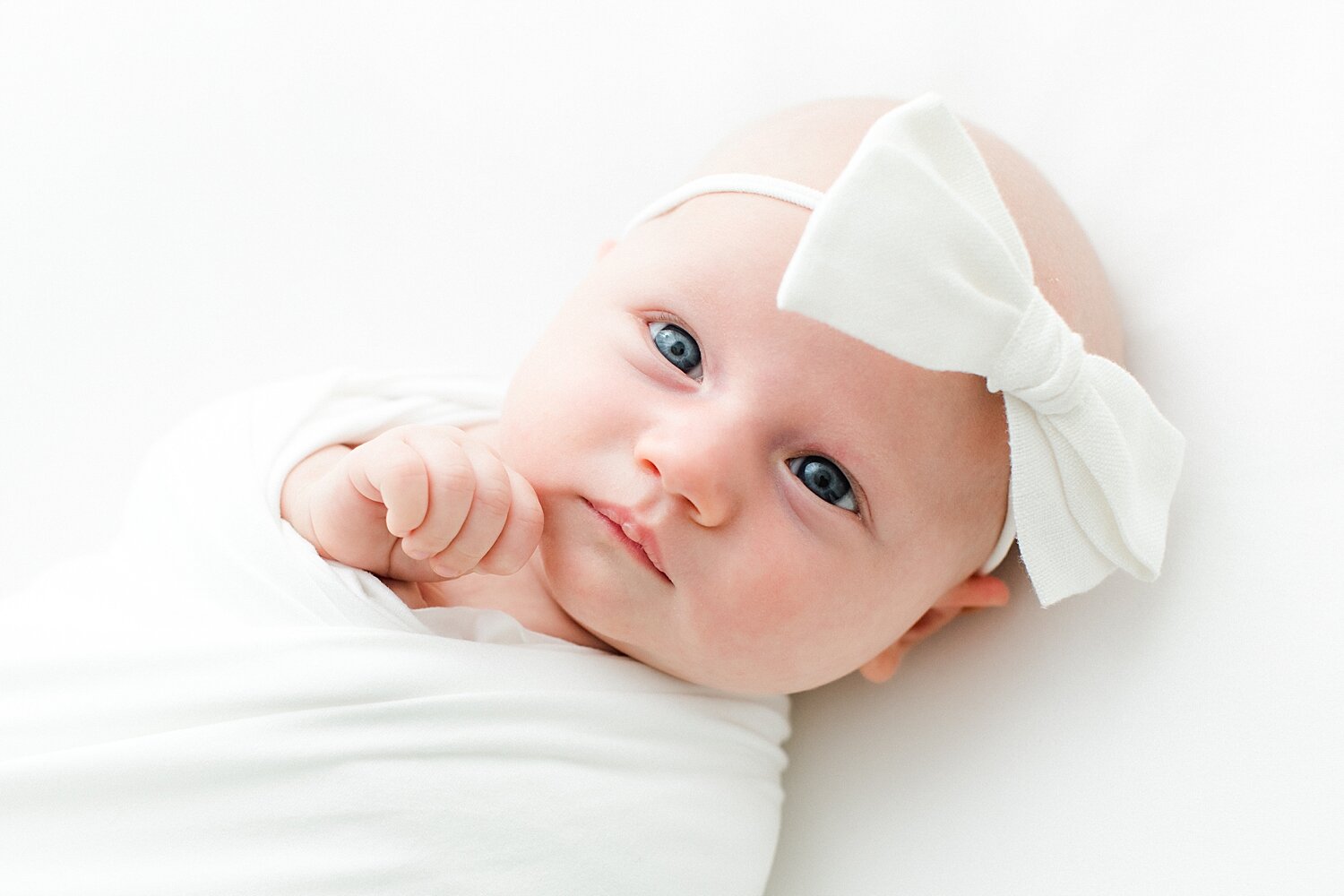 Baby girl with big white bow and white swaddle. Photos by Kristin Wood Photography.