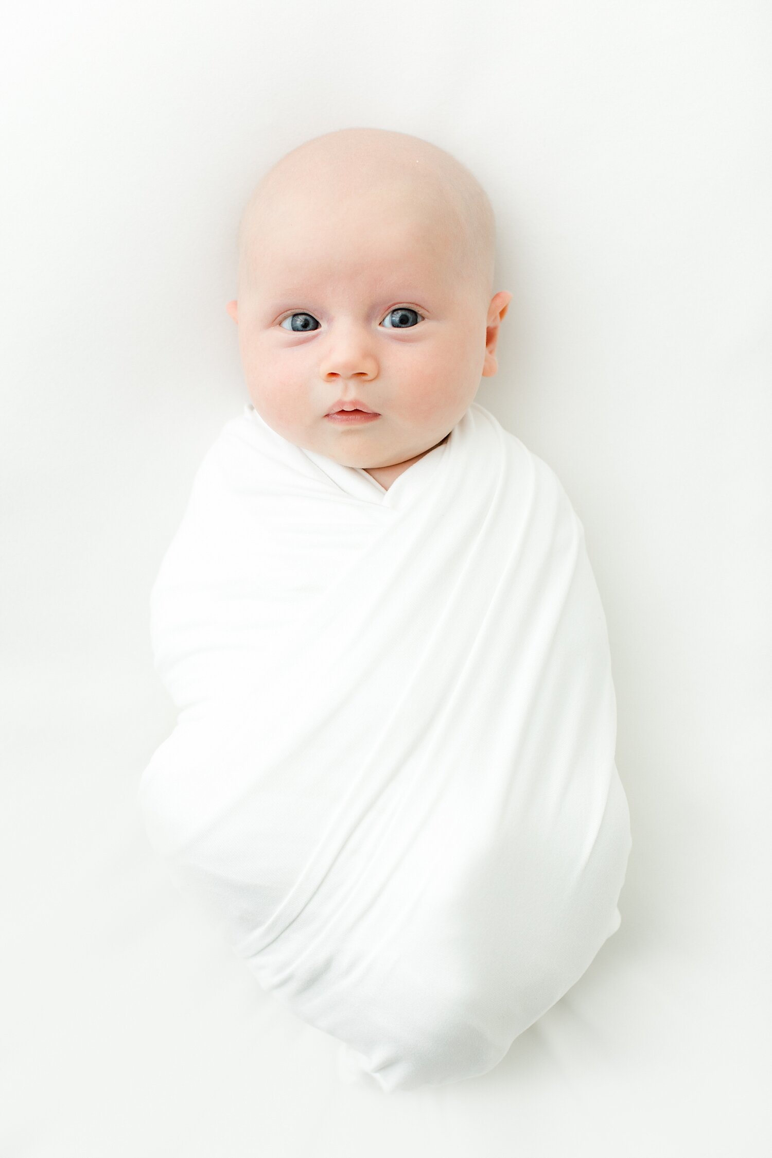 Classic newborn photo of baby girl in a white swaddle on posing beanbag. Photos by Kristin Wood Photography. 