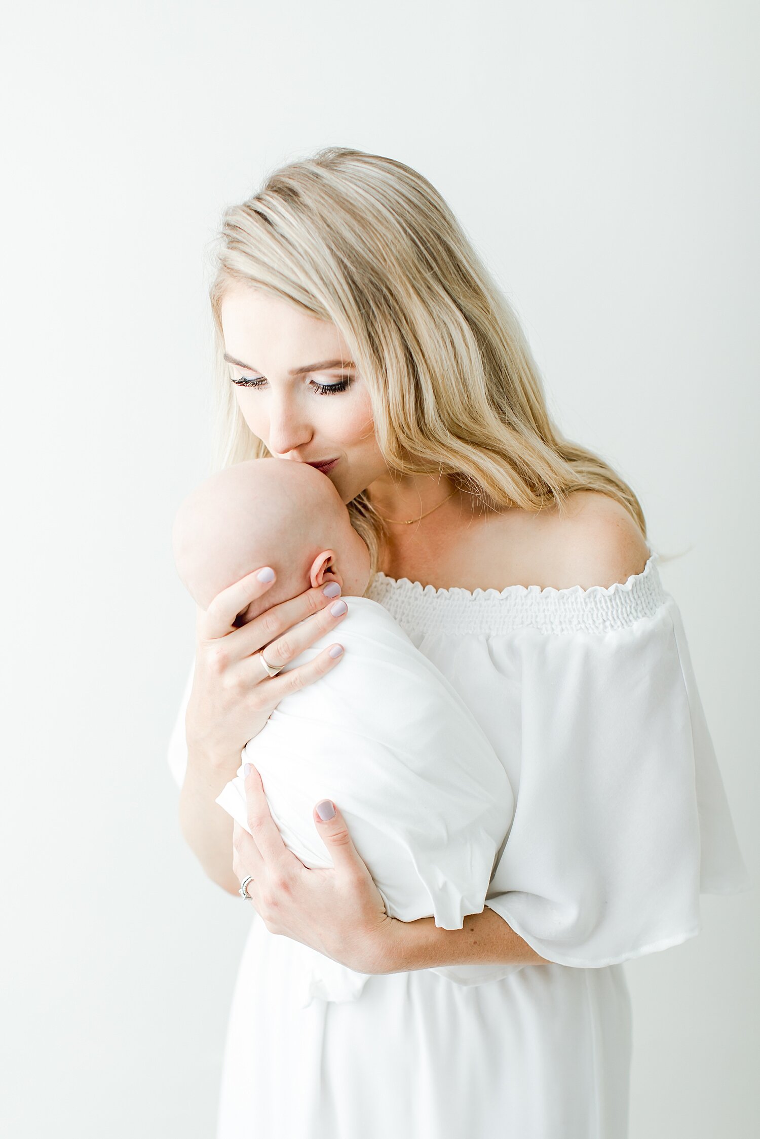 Mama wearing a white dress kissing newborn baby girl. Photos by Greenwich Newborn Photographer, Kristin Wood Photography. 