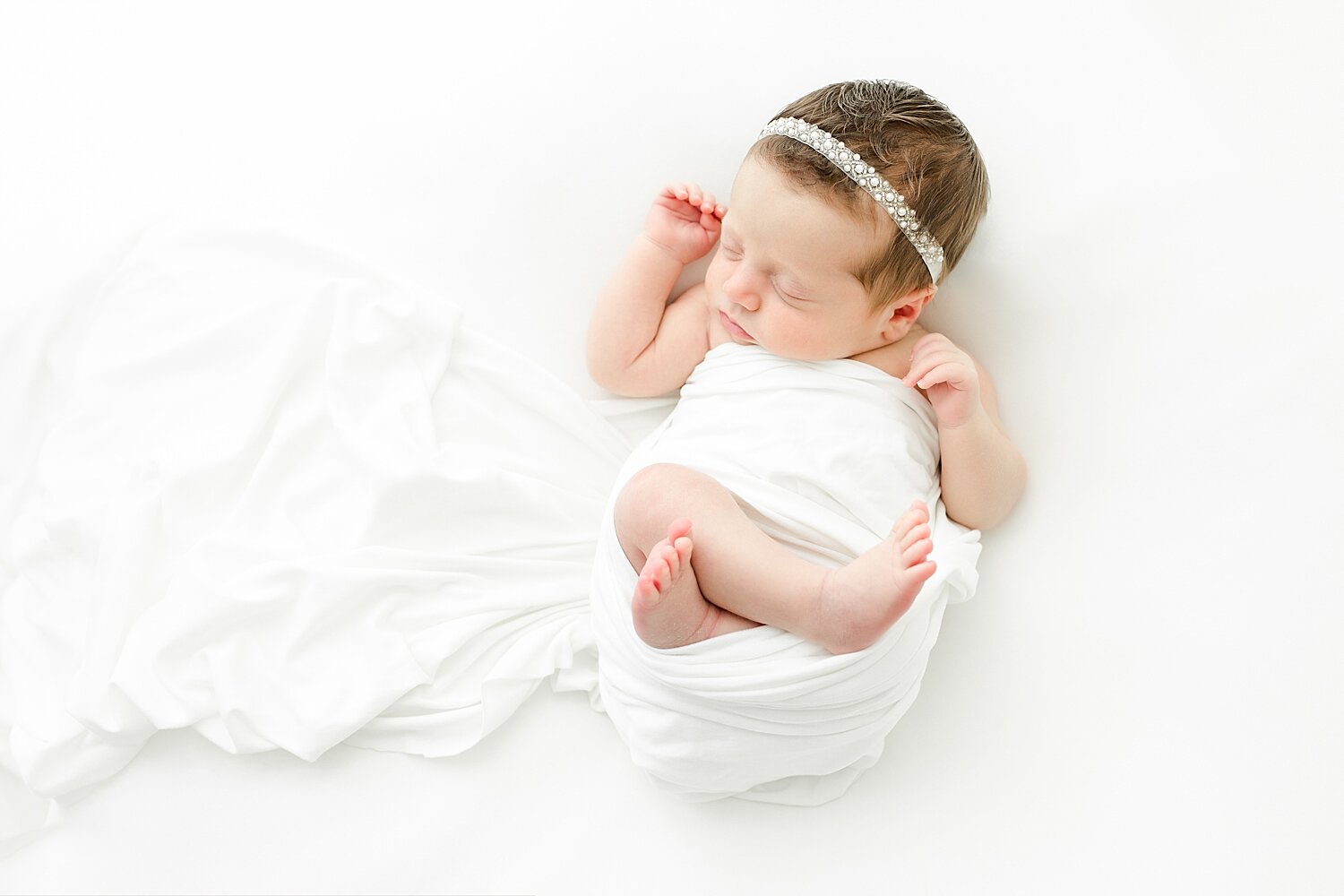 Baby girl swaddled in a white blanket on a white backdrop for newborn session. Photos by Kristin Wood Photography.