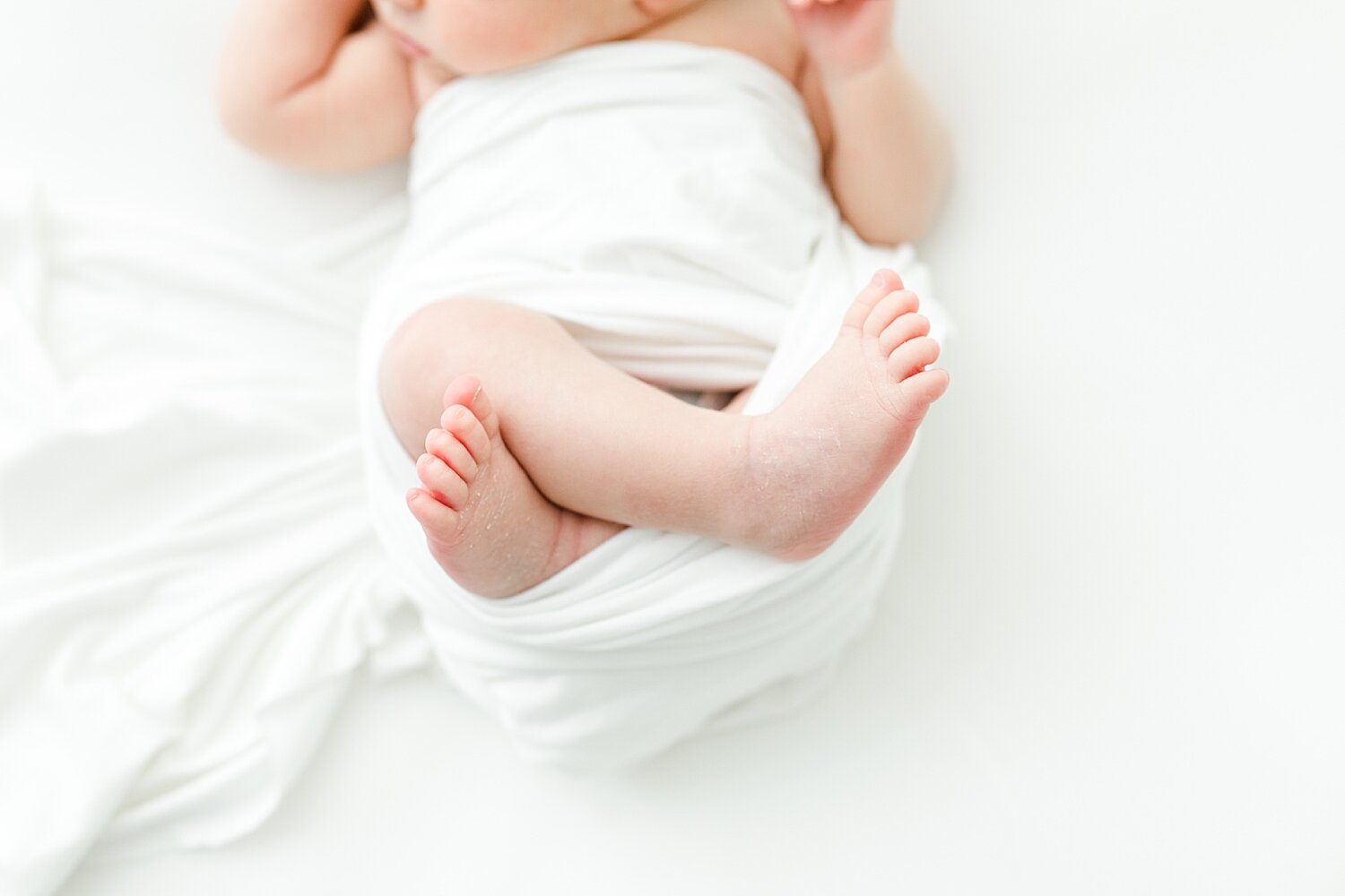 Baby girl swaddled in a white blanket on a white backdrop for newborn session. Photos by Kristin Wood Photography.