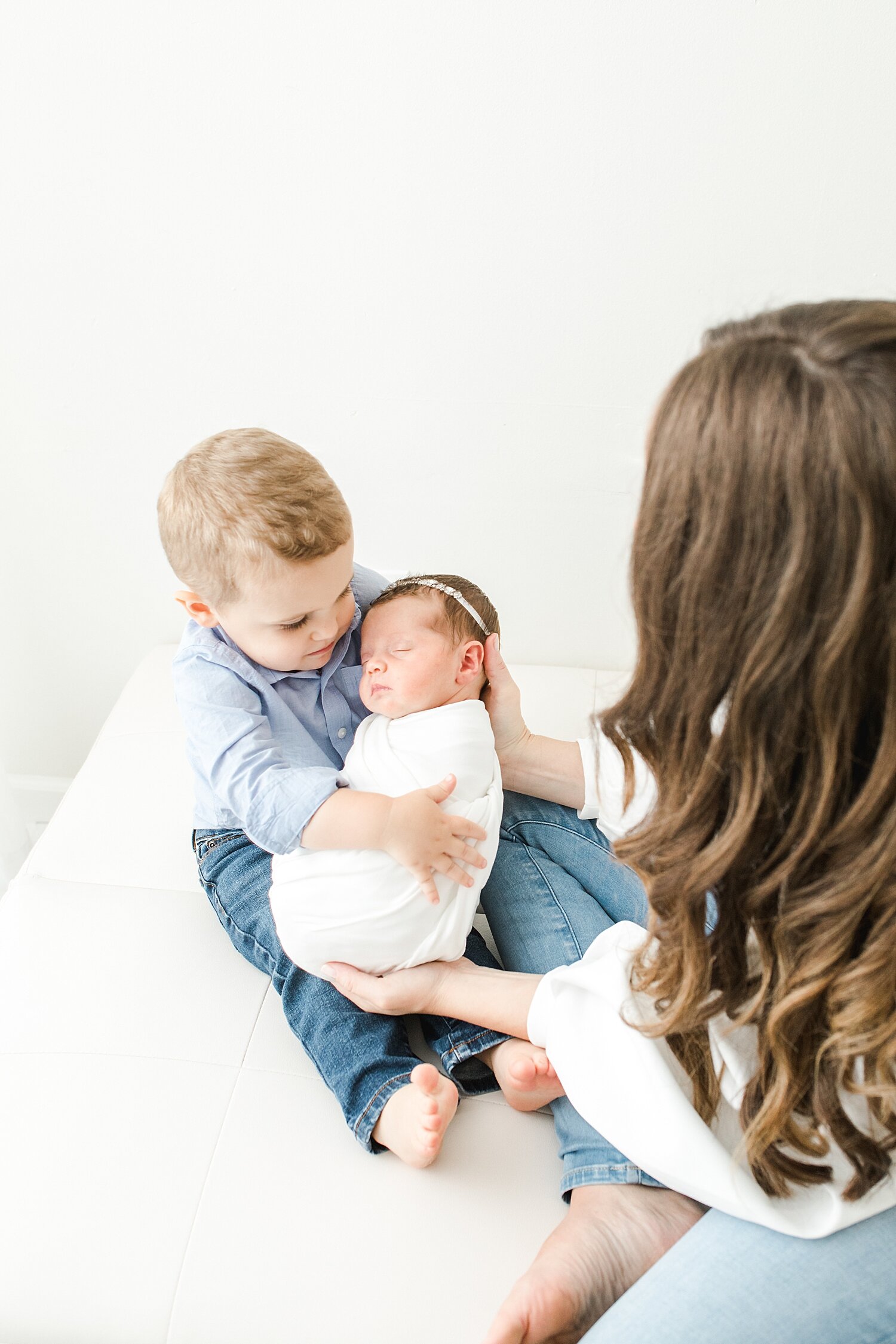 Mom helping big brother hold his baby sister during newborn session. Photos by Kristin Wood Photography.