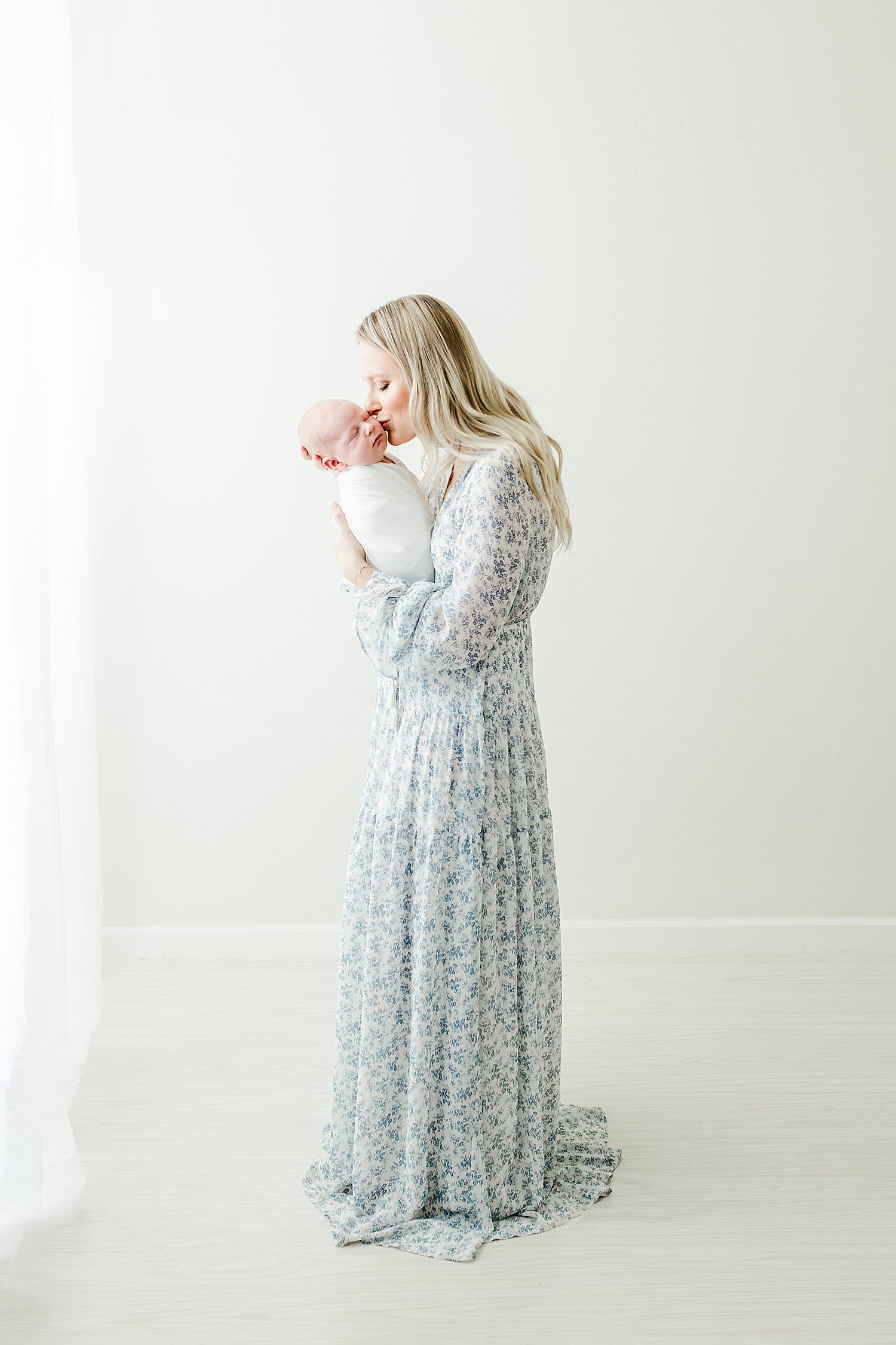 Mom wearing a long blue floral dress for newborn photoshoot. She's kissing her baby boy. Photos by Kristin Wood Photography. 