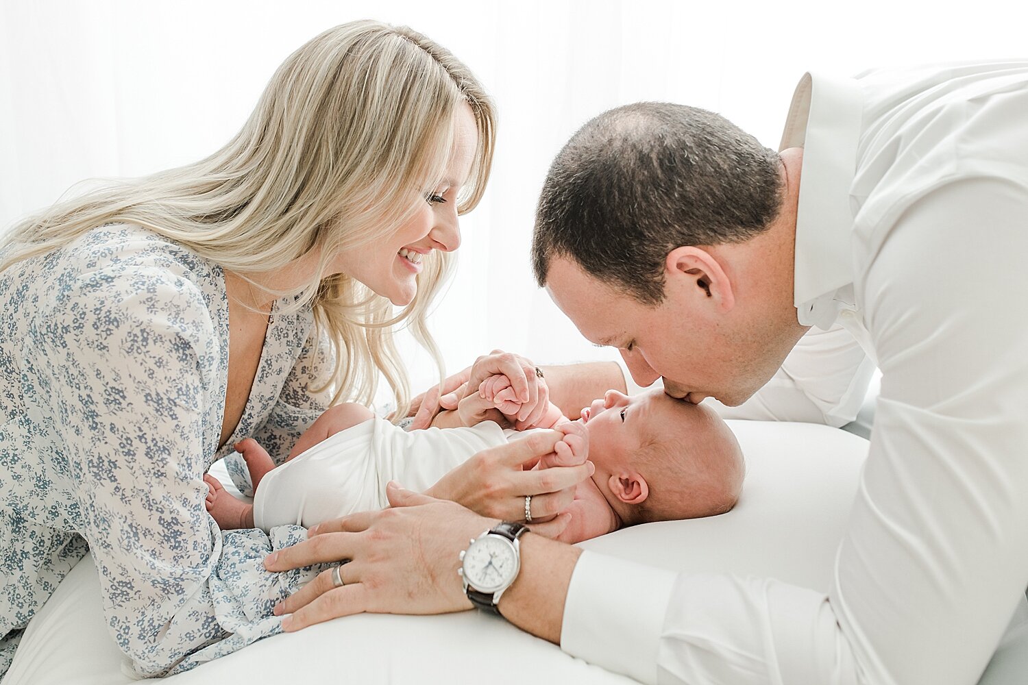 Sweetest newborn session. Dad is giving baby boy a kiss while Mom holds his little fingers. Photos by Kristin Wood Photography.