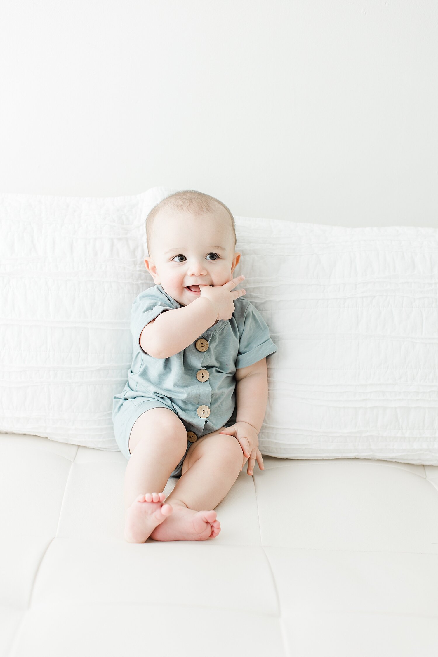 6 month milestone sitter session. Baby has his hands in his mouth smiling. Photos by Kristin Wood Photography.