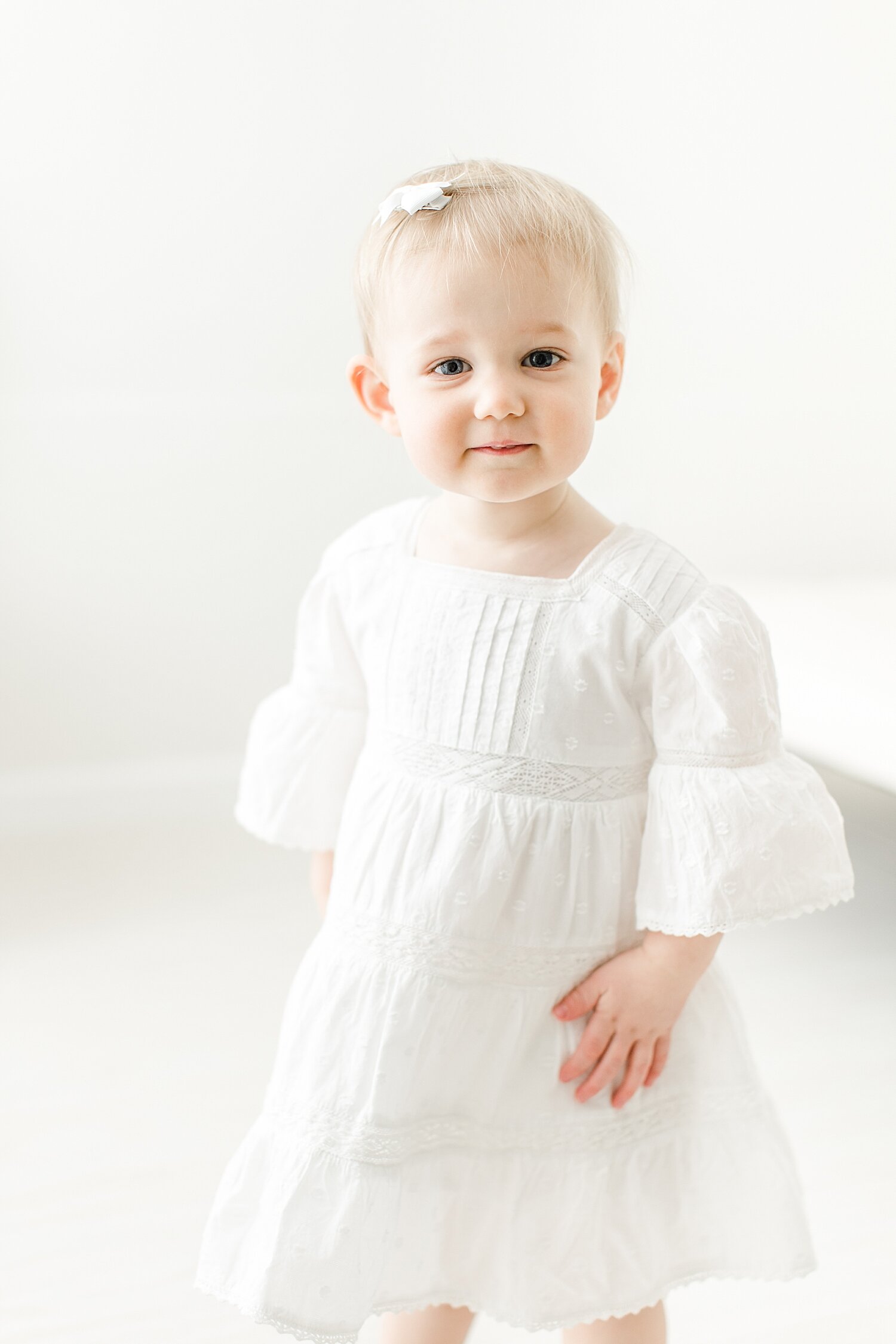 Toddler aged girl standing in beautiful white eyelet dress. Photo by Kristin Wood Photography.