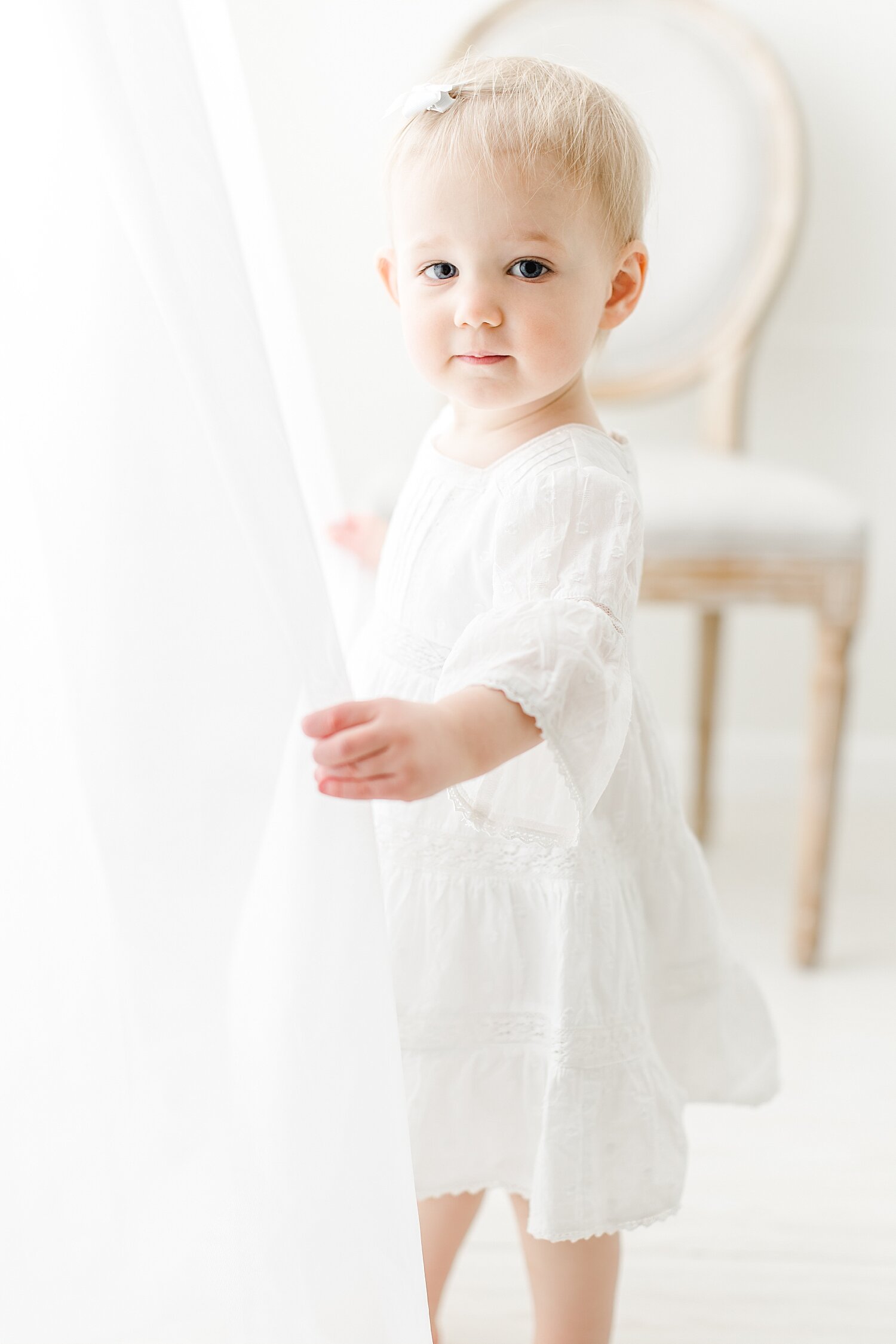 Classic children's portrait of 18 month old little girl playing in curtains. Photo by Kristin Wood Photography.