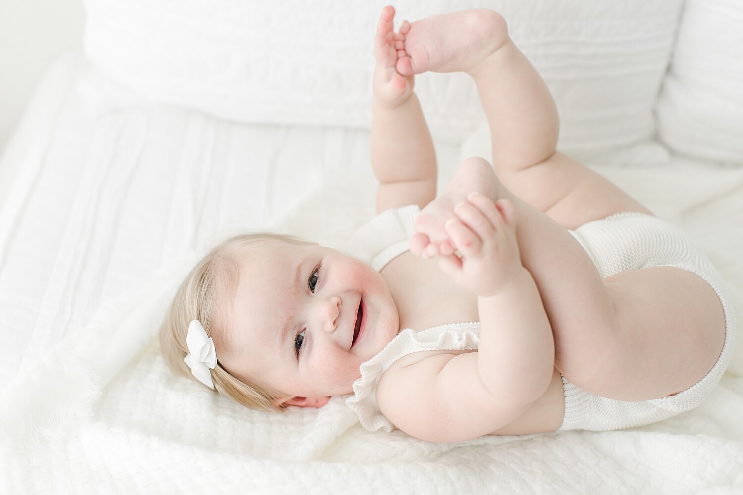 One year old little girl grabbing her feet during her first birthday photoshoot with Kristin Wood Photography.