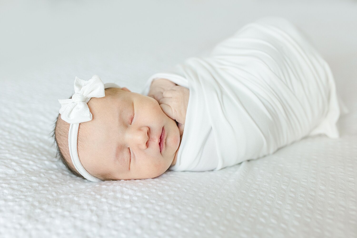 Baby girl swaddled in white with white headband. Photo by Kristin Wood Photography.