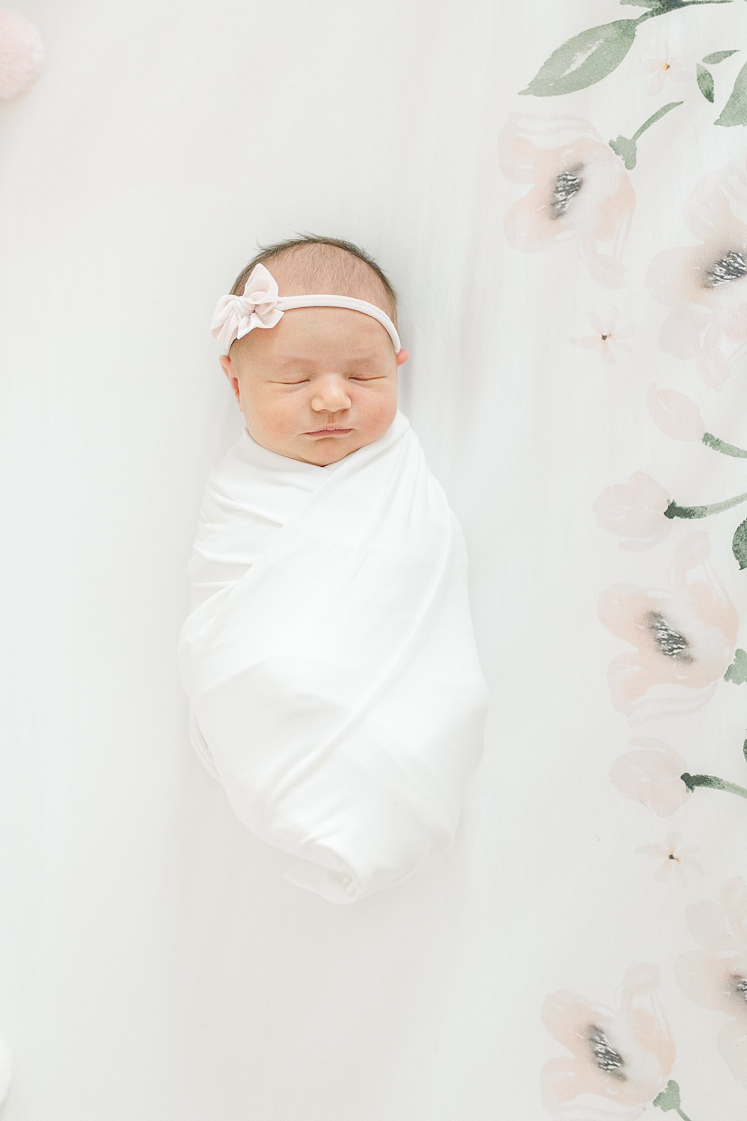 Newborn baby girl laying in crib on floral sheet. Photo by Kristin Wood Photography.