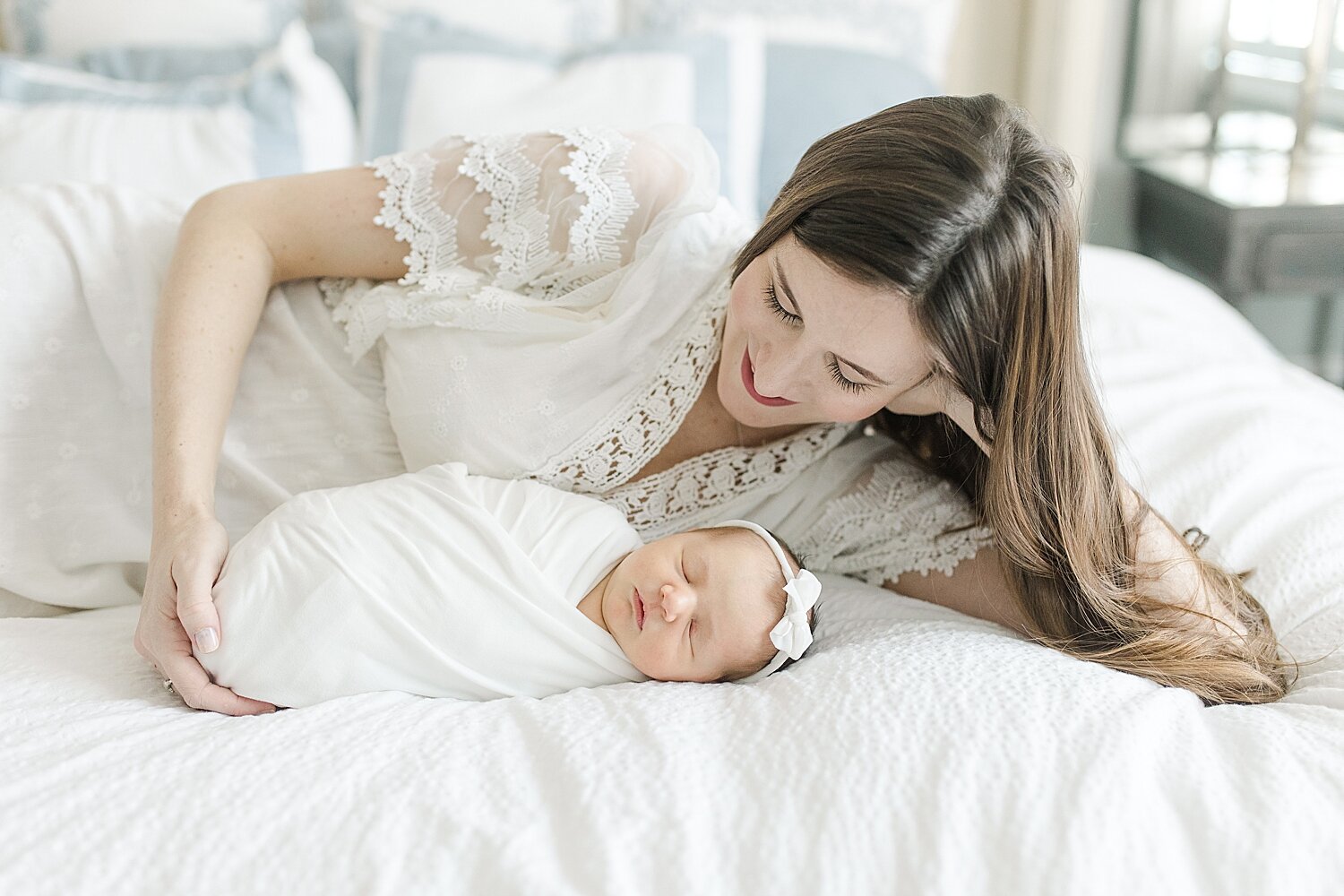 Mom curled up with her baby girl on the bed during their in-home lifestyle newborn session with Kristin Wood Photography.