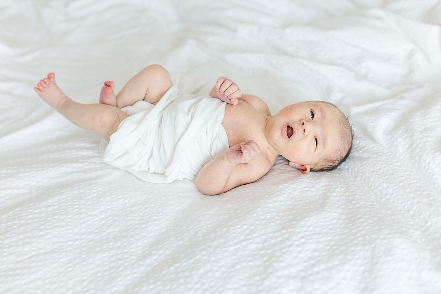 Baby girl swaddled in a white blanket stretching out her legs. Photo by Kristin Wood Photography.