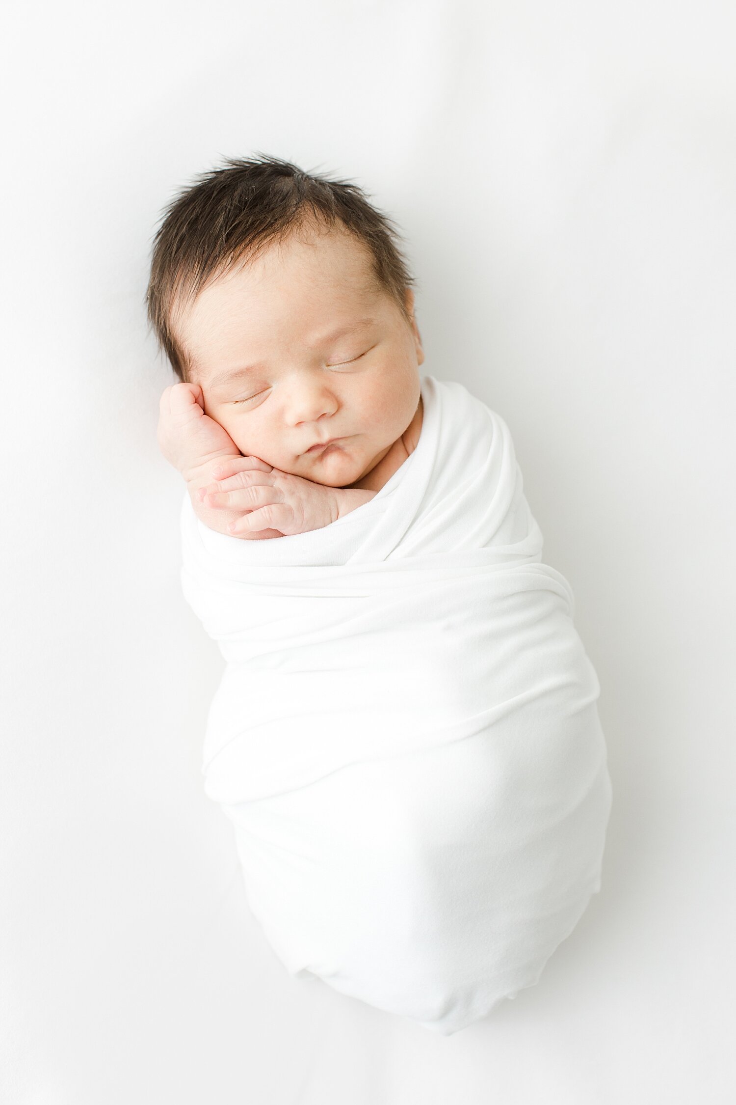 Baby boy swaddled in white with his hands up by his face. Photo by Fairfield County, CT Newborn Photographer, Kristin Wood Photography.