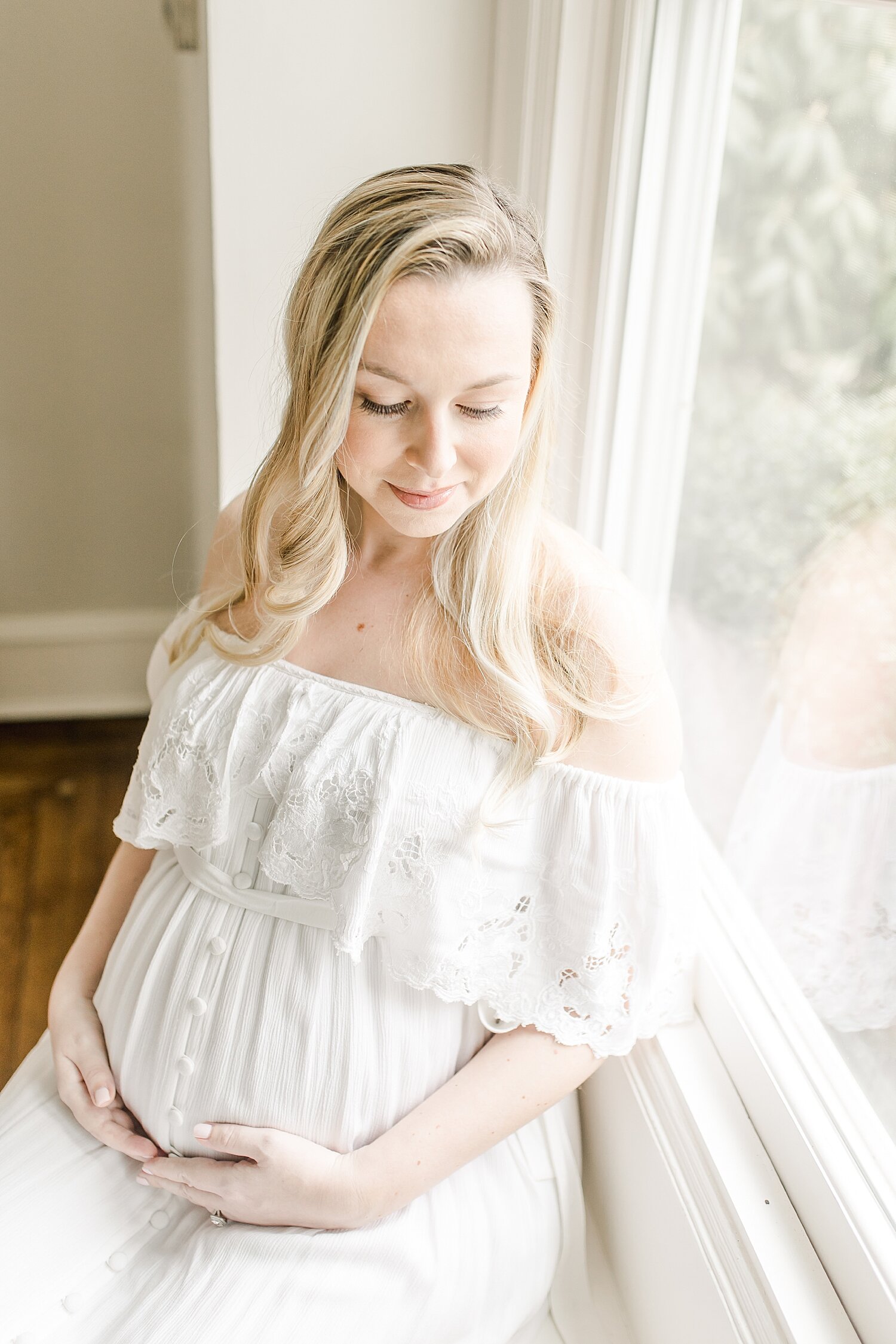 Pregnant mom wearing fillyboo maternity dress sitting in window seat. Photo by Kristin Wood Photography.