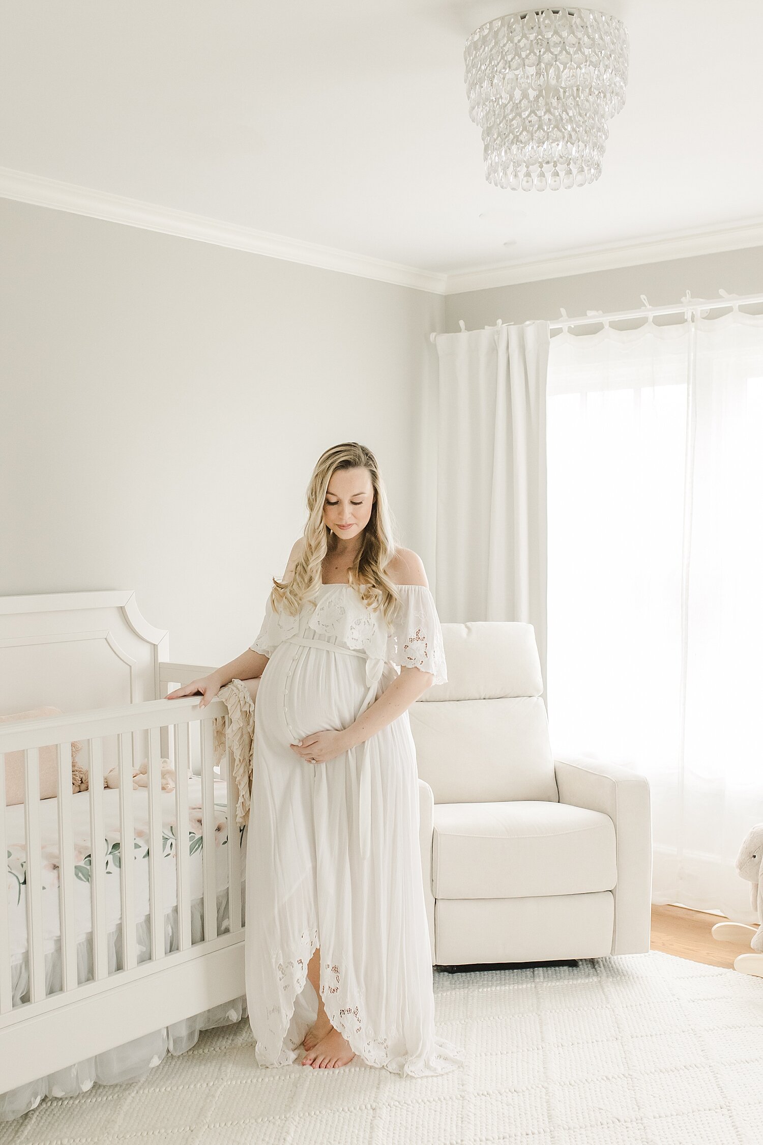 Mom standing in front of crib in baby girl's nursery. Maternity photos by Kristin Wood Photography.