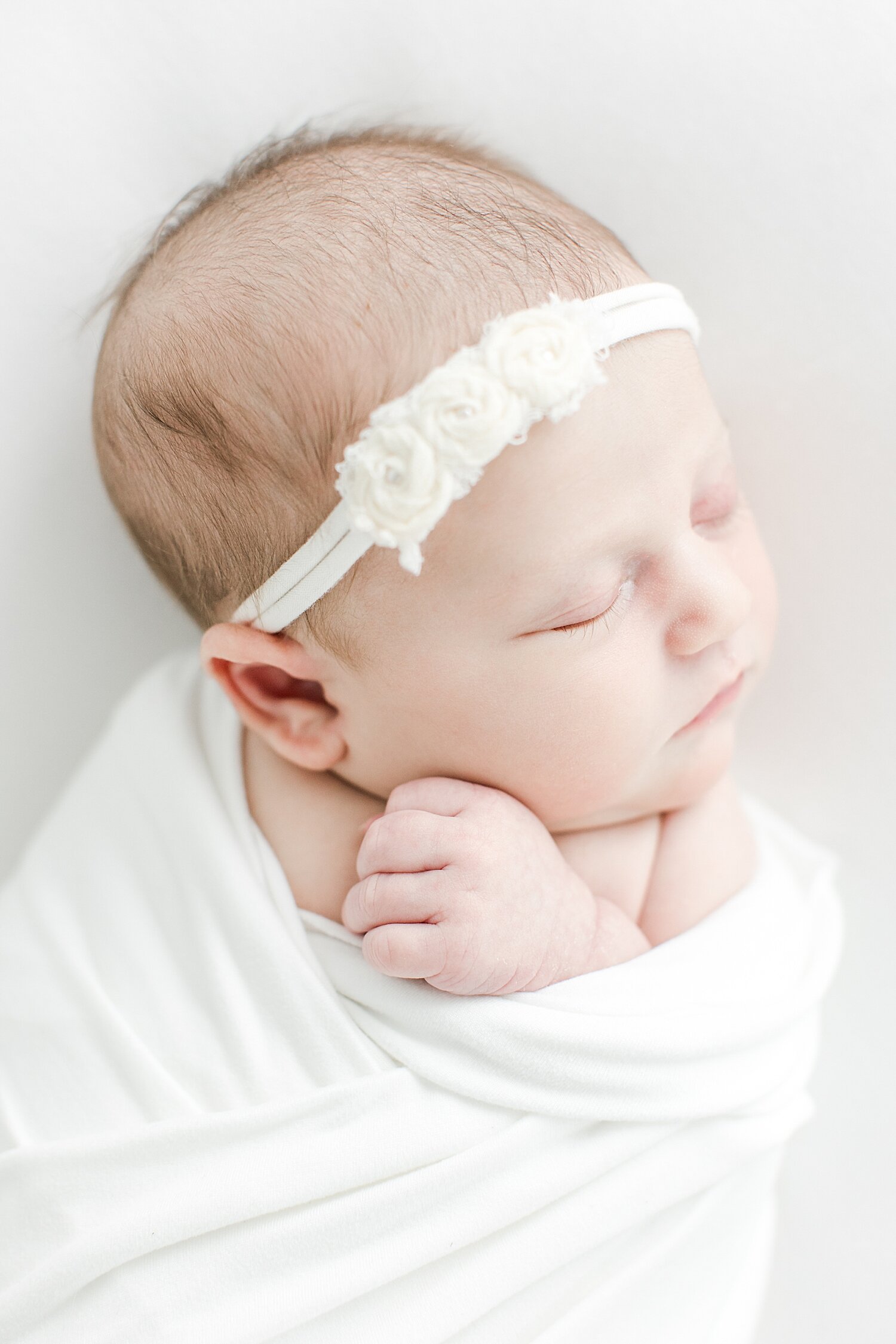 Baby girl swaddled in white with a white headband for newborn photos with Kristin Wood Photography in Westport, CT. 