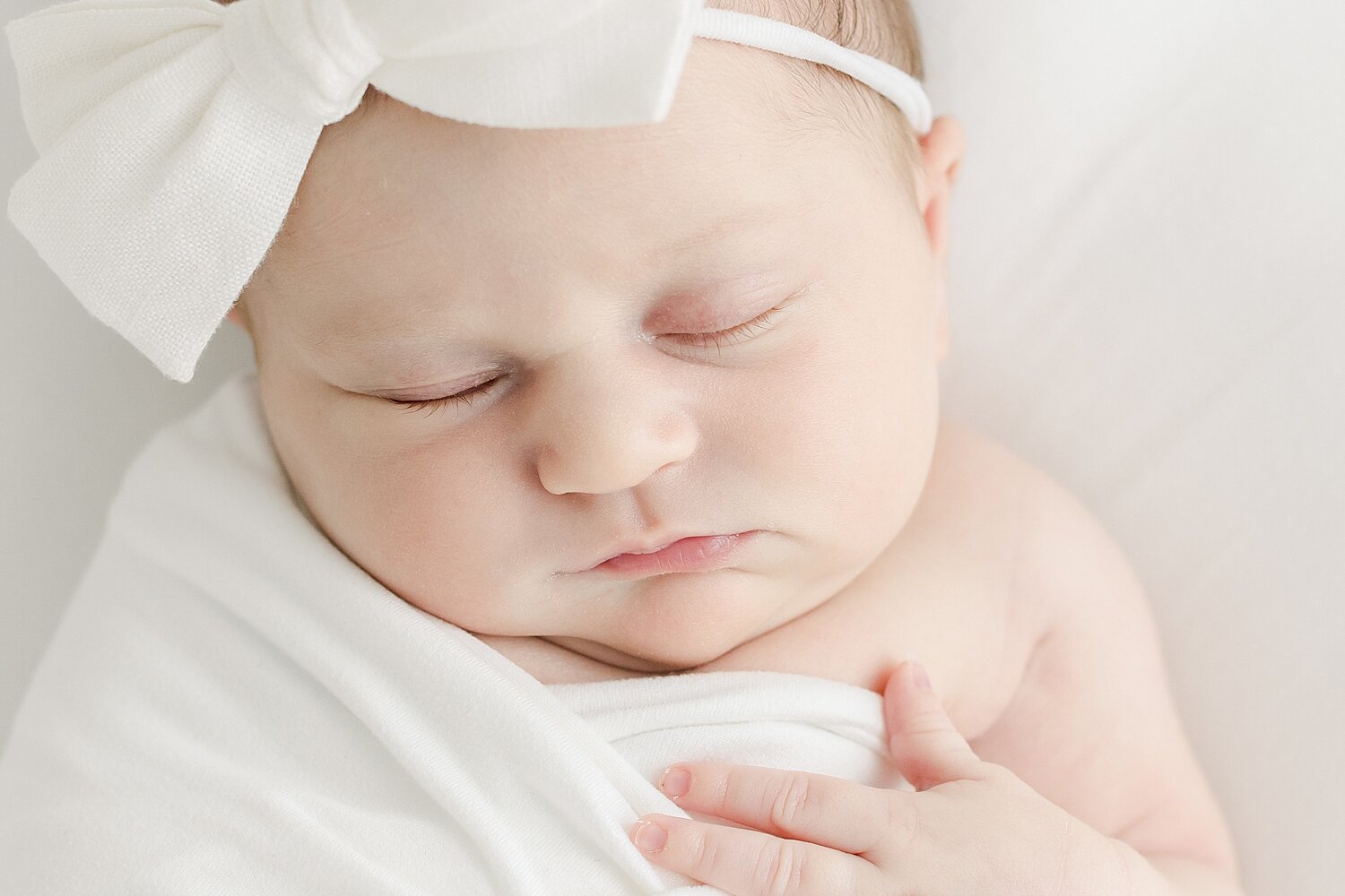 Baby girl swaddled in white with a white headband for newborn photos with Kristin Wood Photography in Westport, CT. 
