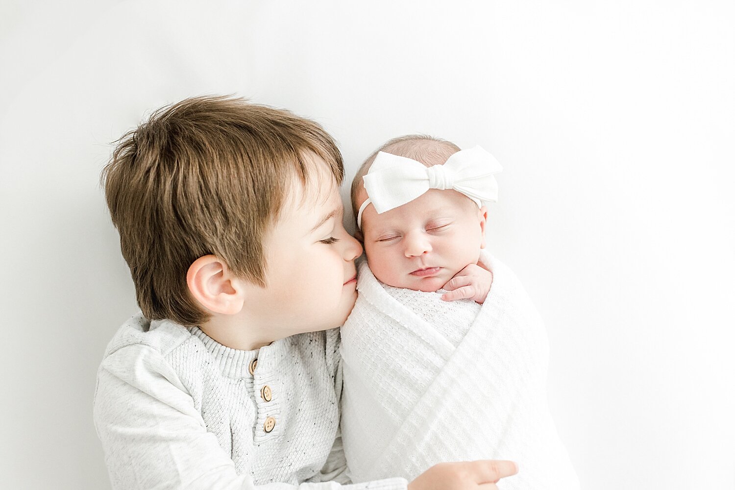 Big brother giving baby sister a kiss. Kristin Wood Photography is sharing tips for how to have a successful newborn session with a toddler.