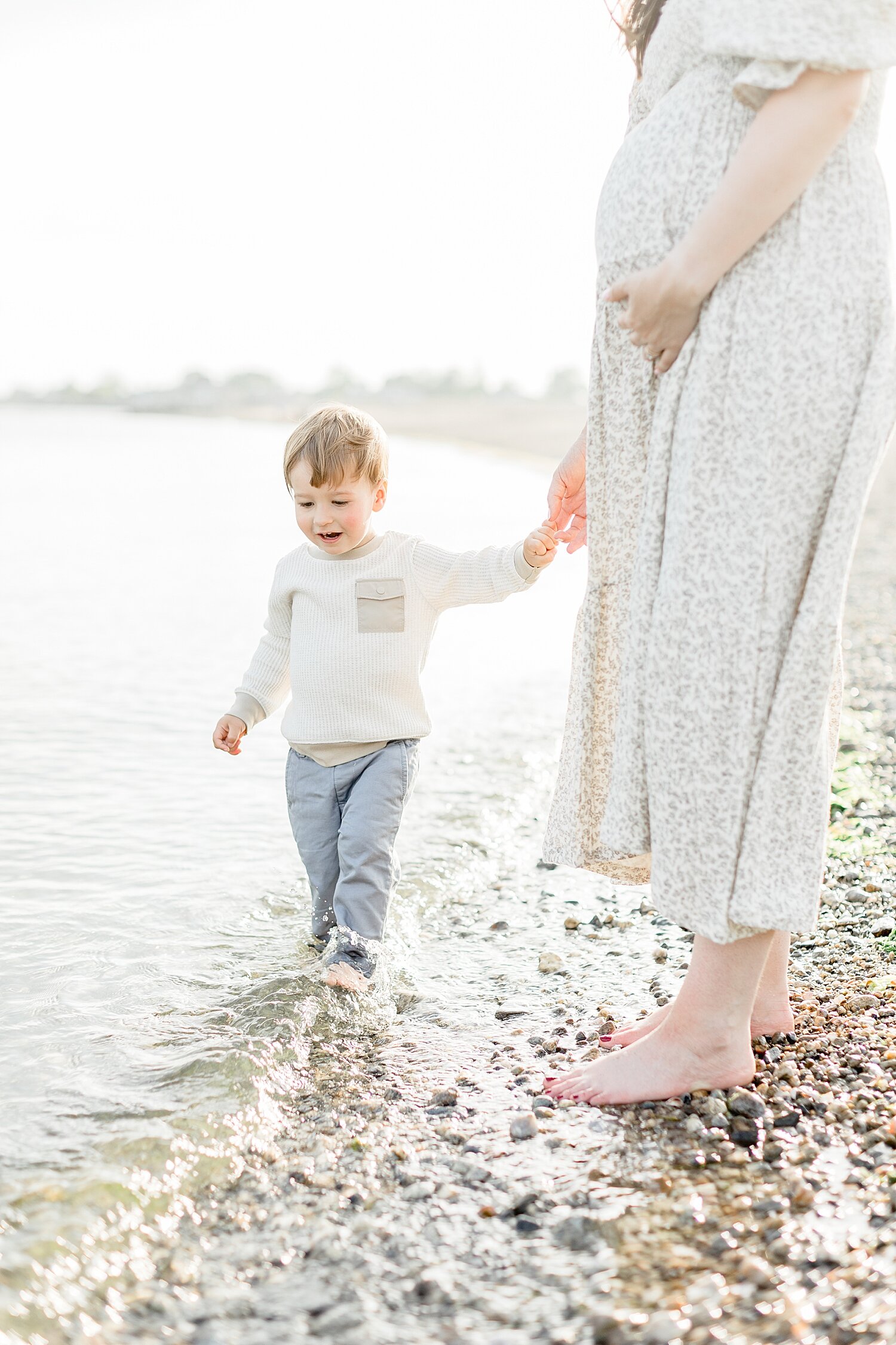 Mom holding sons hand as he walks by the water at Sherwood Island. Photo by Kristin Wood Photography.