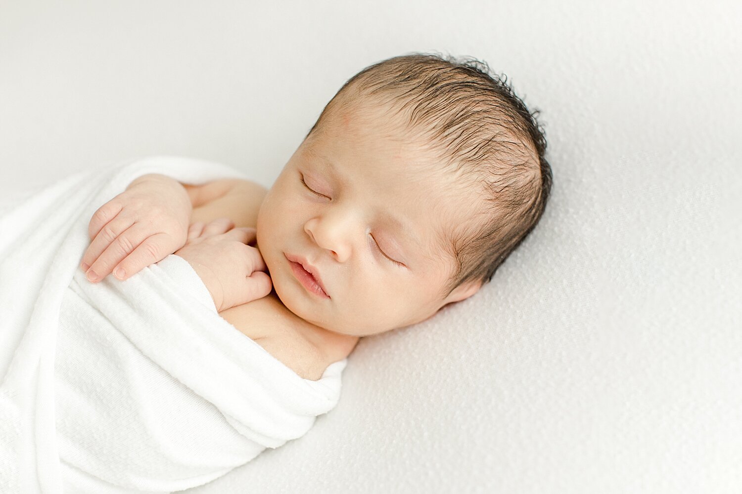 Newborn baby sleeping swaddled in white. Photo by Kristin Wood Photography.