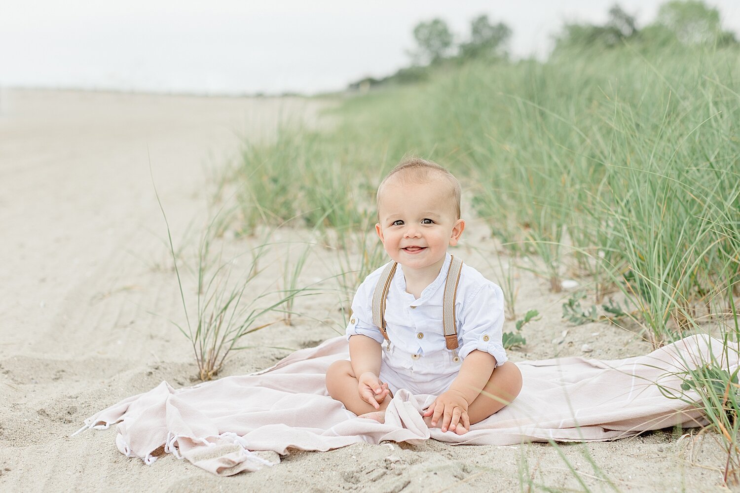 One year old little boy sitting on the beach at Sherwood Island for first birthday photoshoot with Kristin Wood Photography.