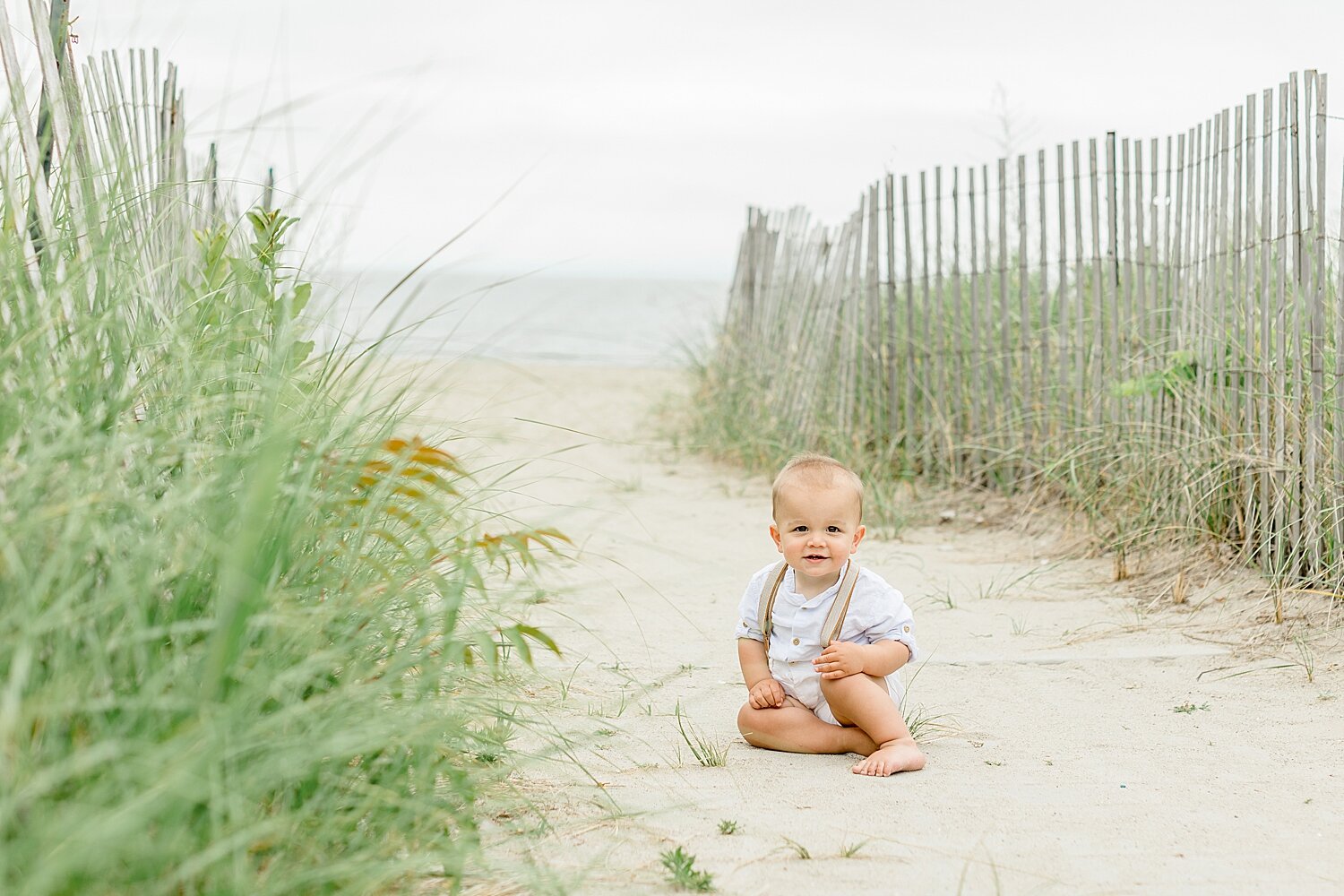 One year old little boy sitting on the beach at Sherwood Island for first birthday photoshoot with Kristin Wood Photography.
