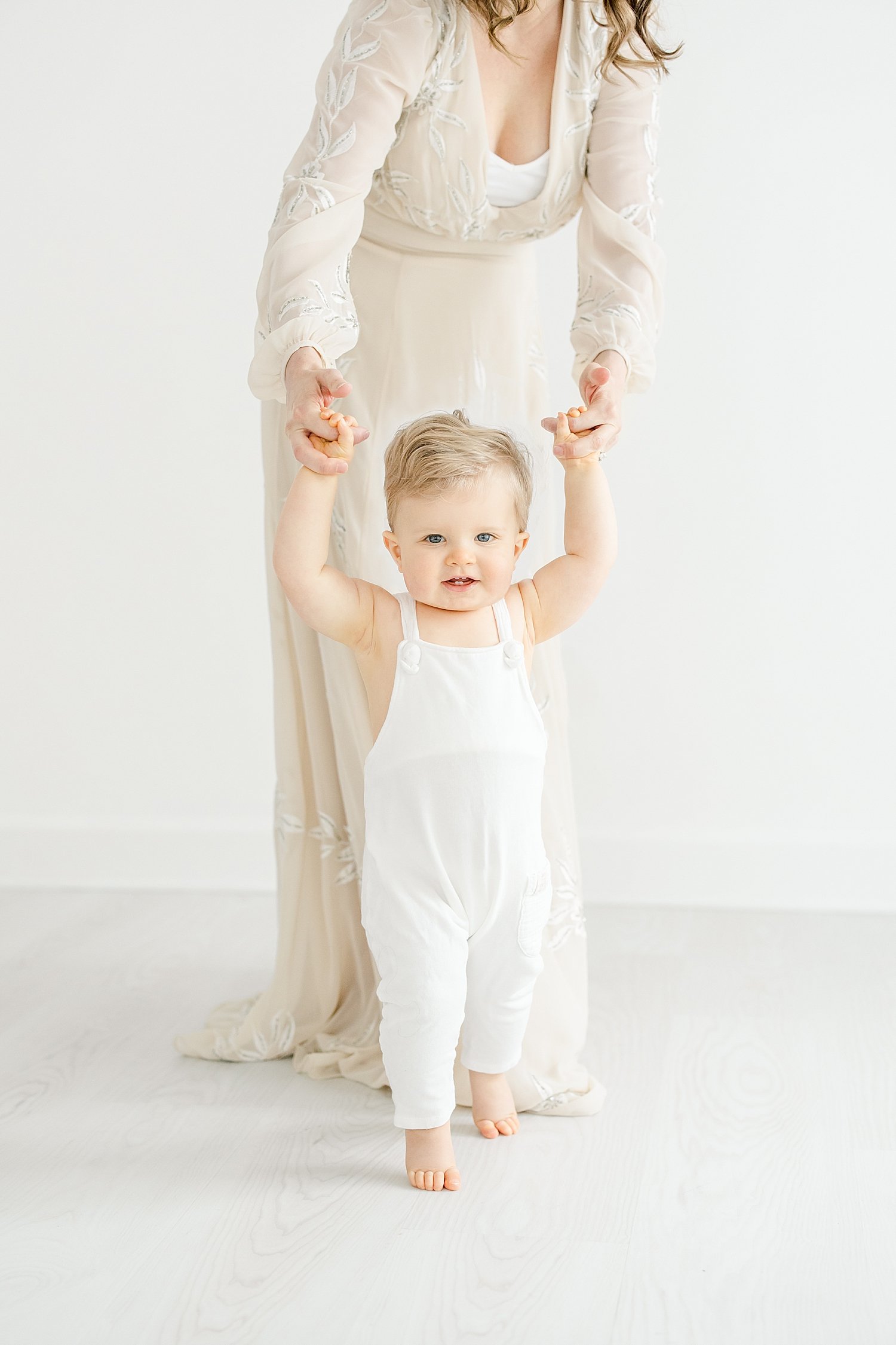 One year old little boy holding his Moms hands walking. Photo by Kristin Wood Photography.