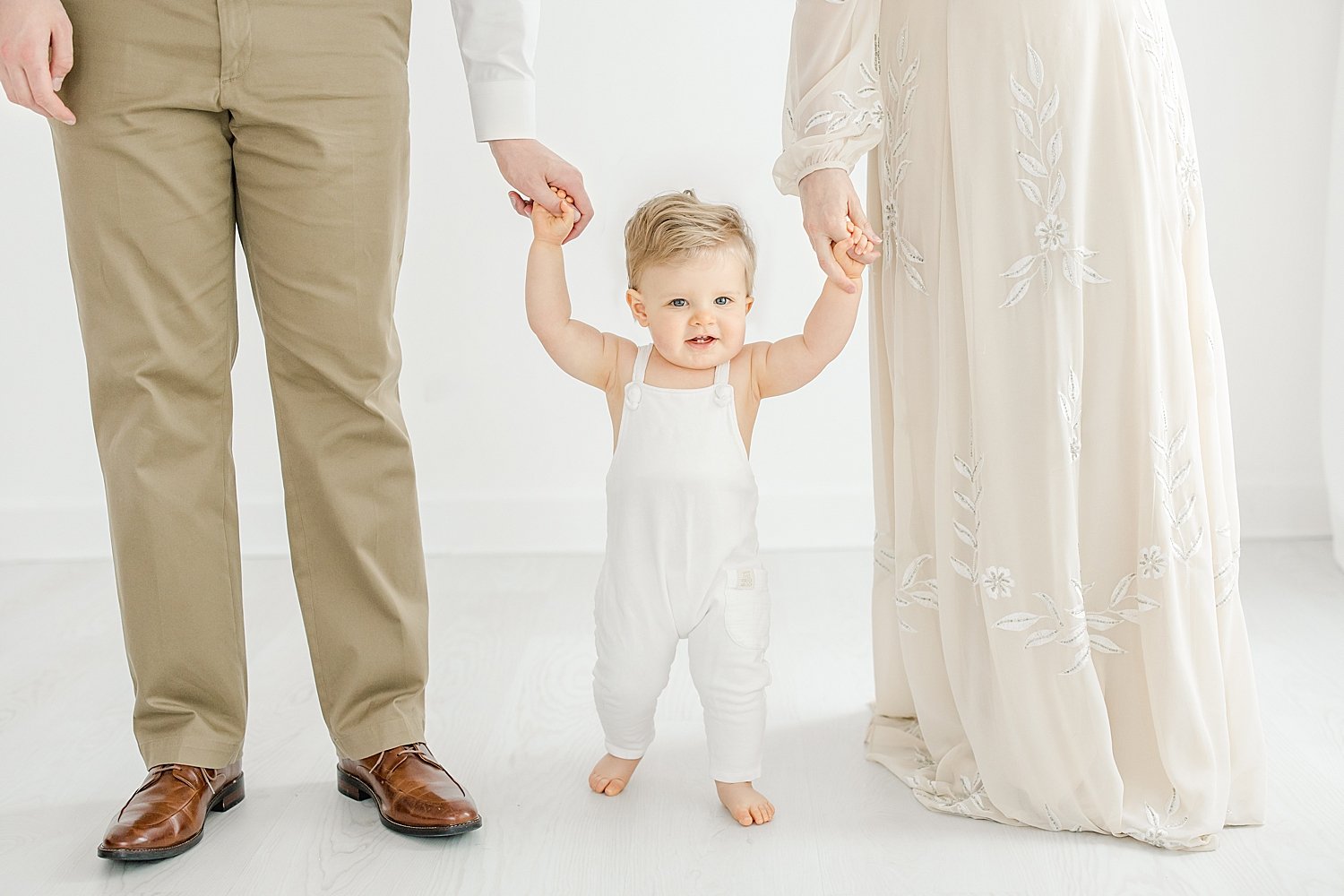 One year old little boy holding his Mom and Dad's hands walking. Photo by Kristin Wood Photography.