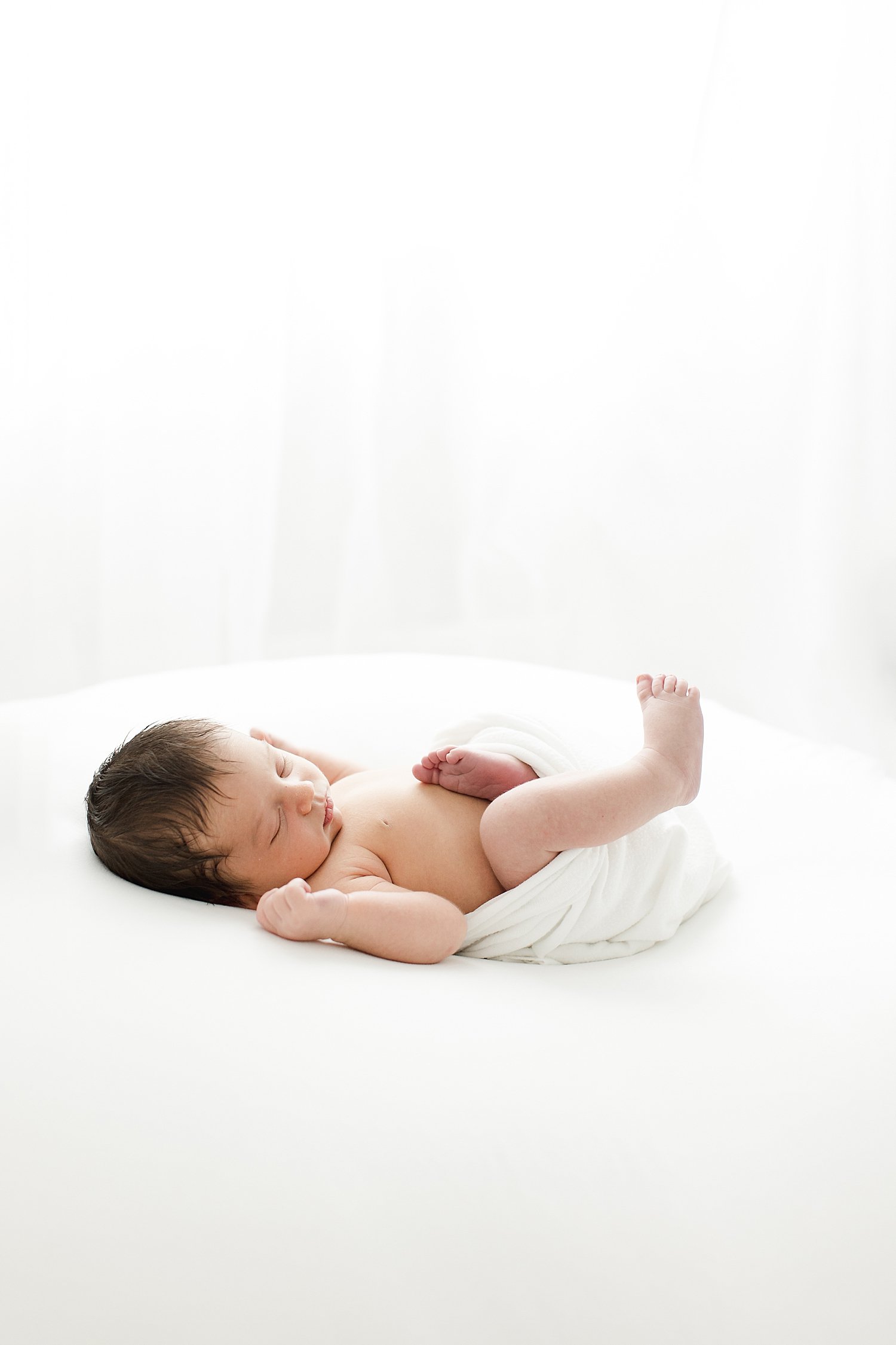 Baby boy swaddled in white laying on white blanket | Kristin Wood Photography