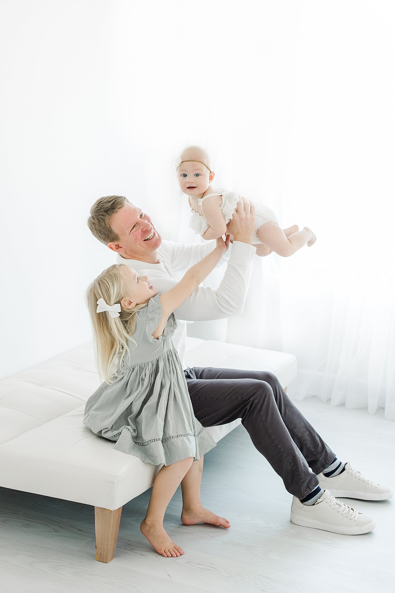 Dad holding youngest daughter up while oldest sits beside him | Kristin Wood Photography