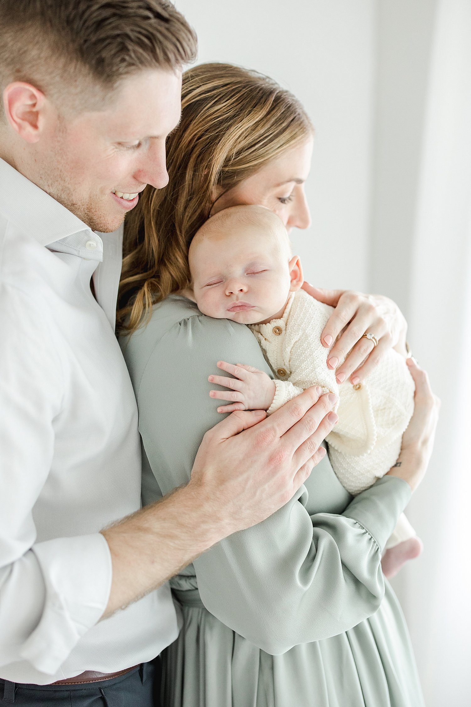 Baby sleeping on Mom's shoulder with Dad looking at them. Photo by Fairfield County, CT newborn photographer, Kristin Wood Photography.
