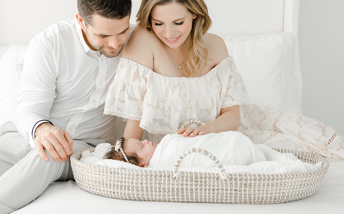 Mom and Dad looking over baby in Moses basket during newborn photos with Kristin Wood Photography.