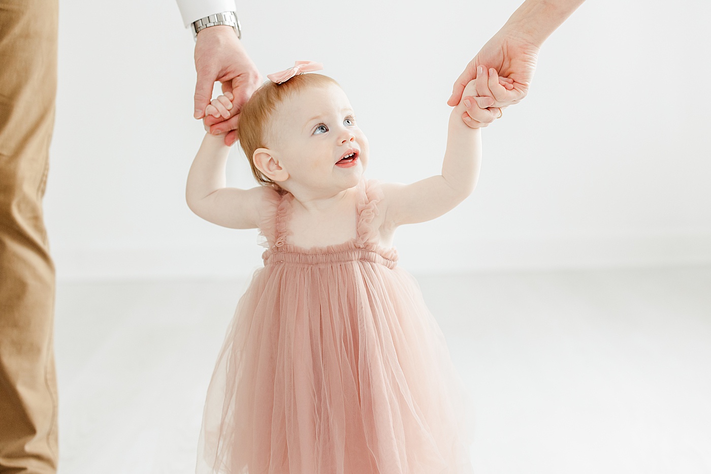 One year old holding mom and dad's hands during photos with Kristin Wood Photography.