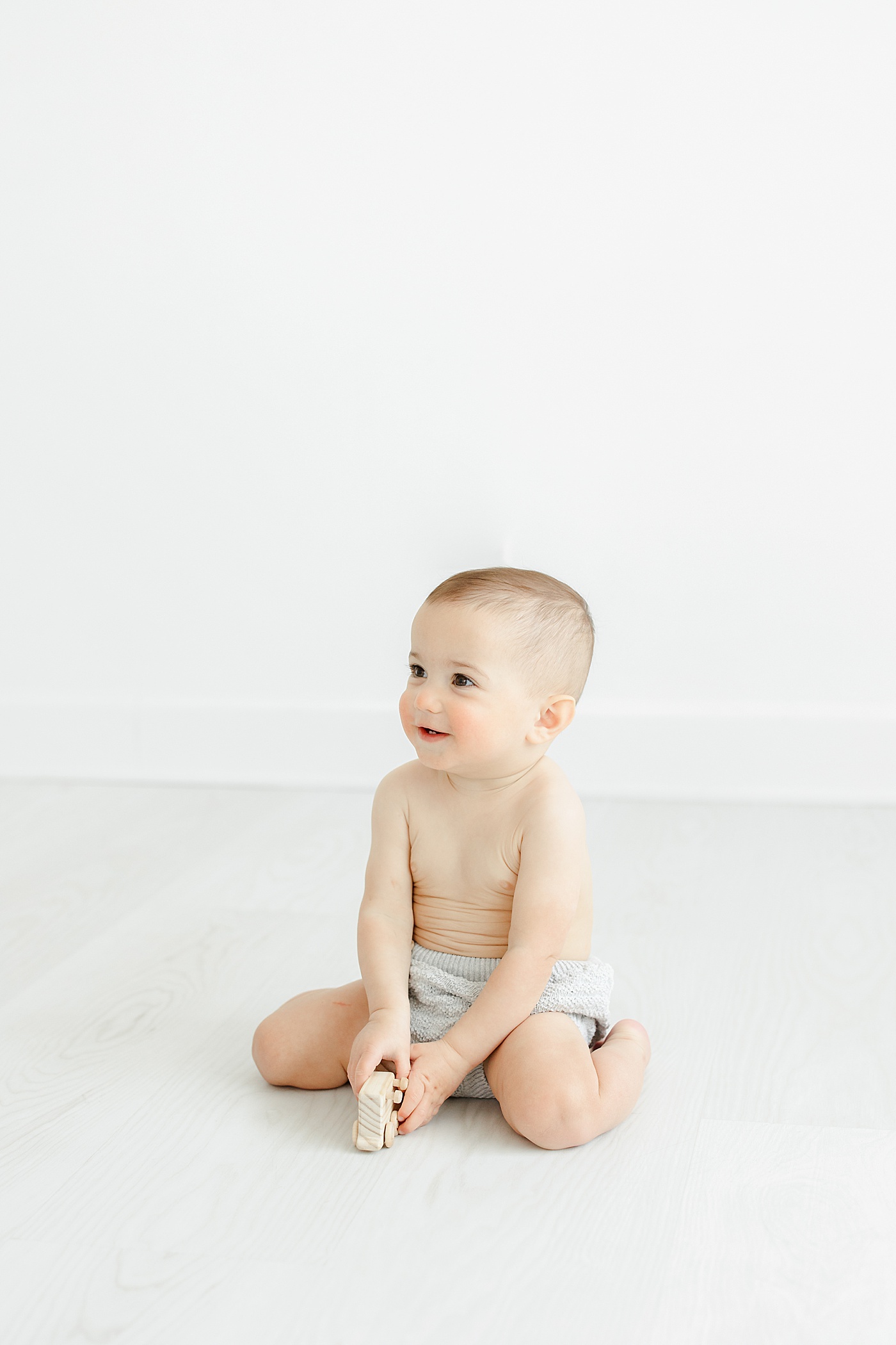 One year old boy playing with wood truck during first birthday photoshoot with Kristin Wood Photography.